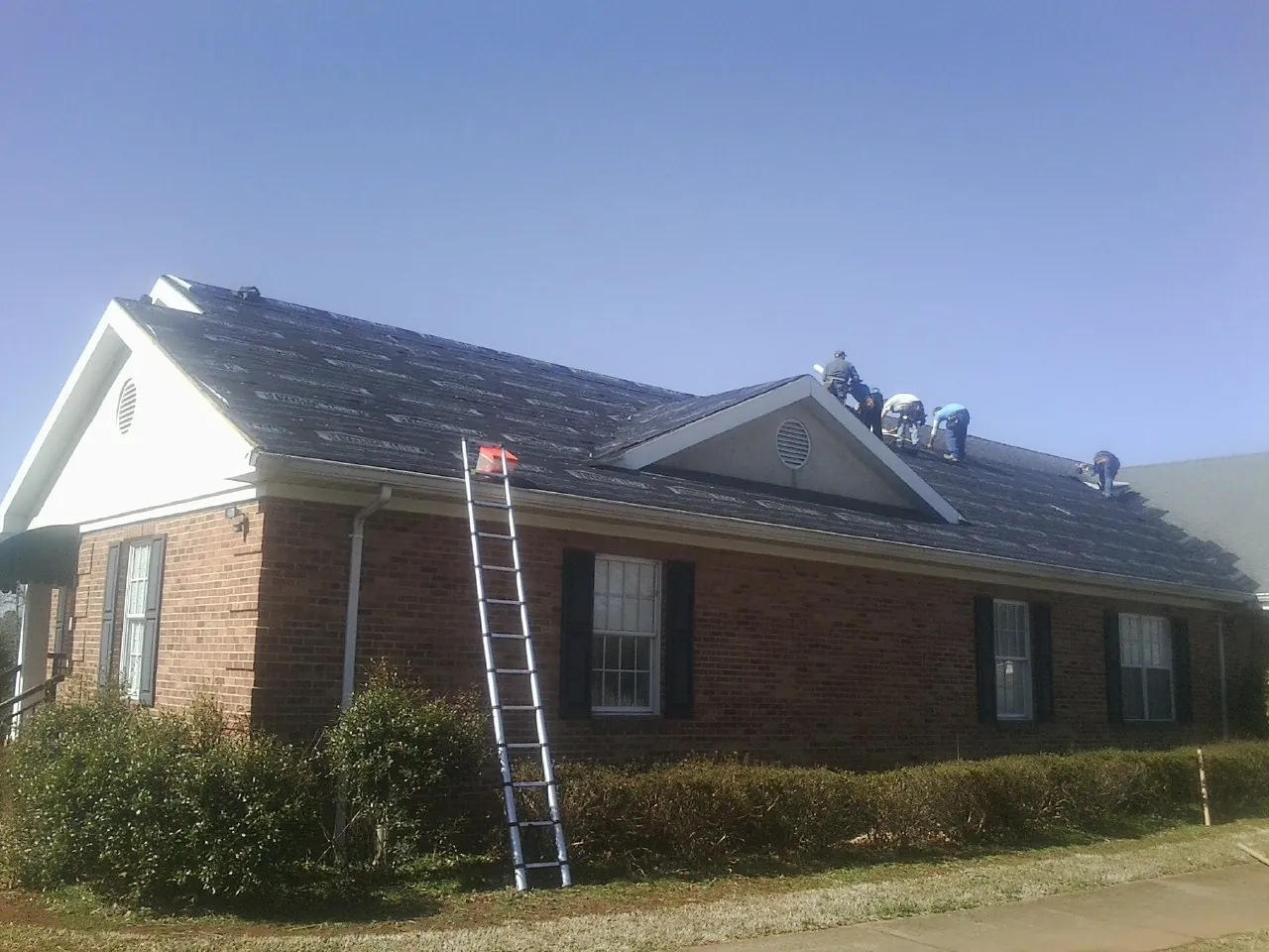Crew tearing shingles off a brick ranch roof with a ladder set — Metal Roof Repair work by our crew in Cottondale