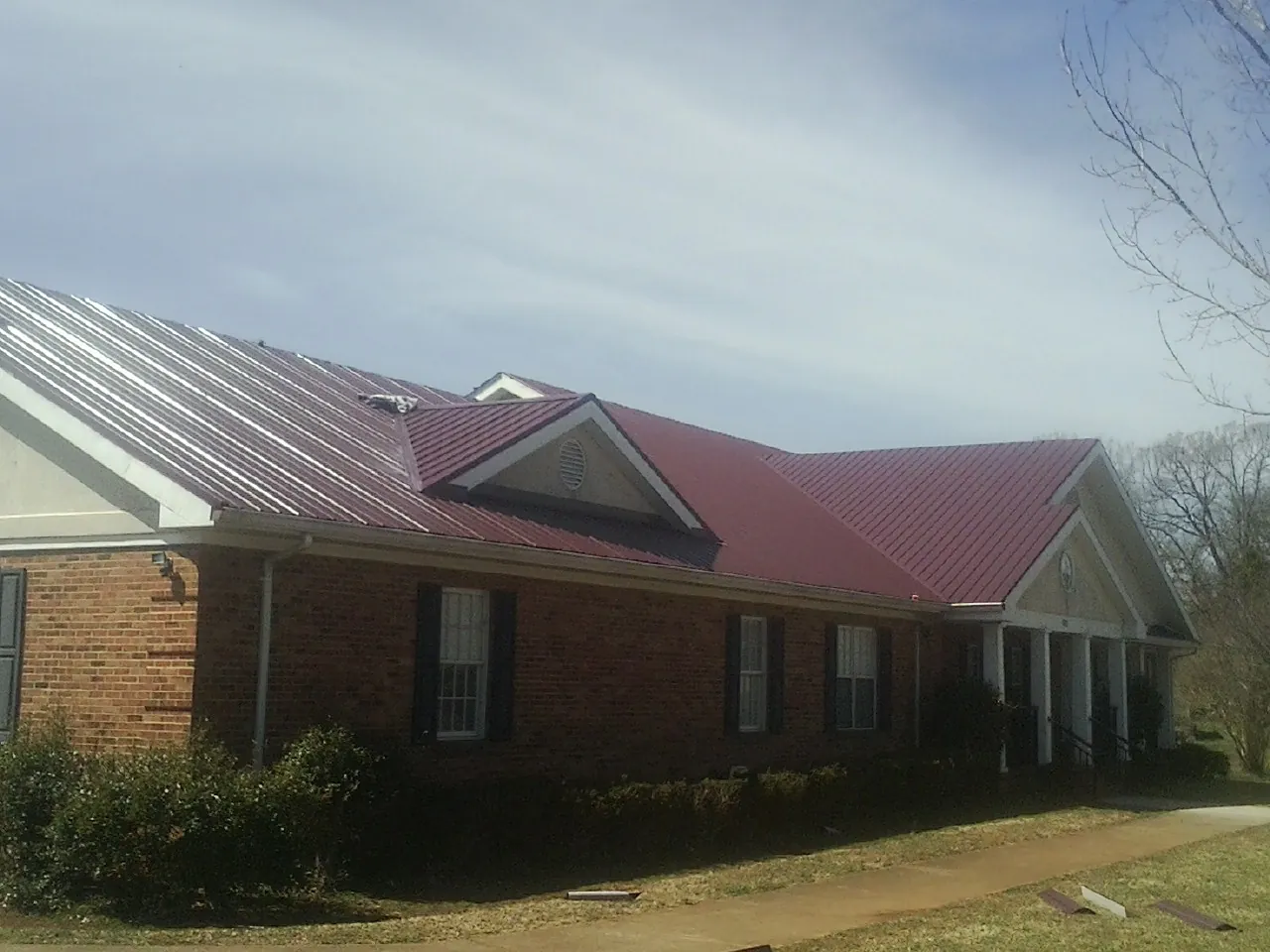 Red metal roof with gabled entries on a long brick building, from a Hail Damage Roof Repair job in Cottondale