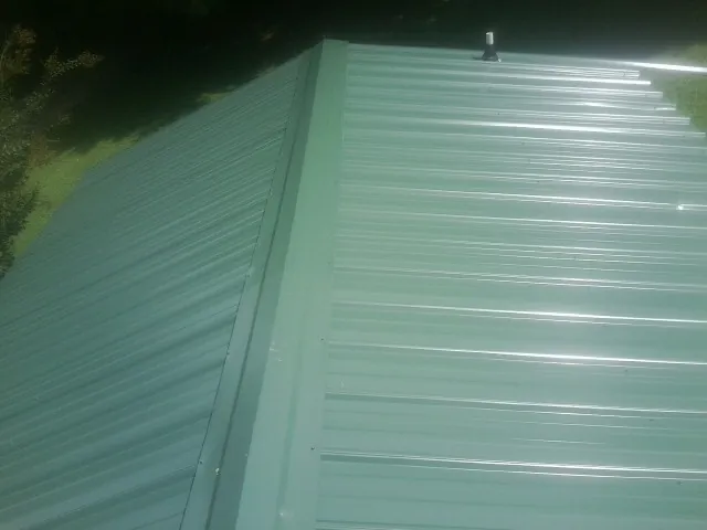 New green metal panels meeting at the ridge of a roof — Flat Roof Repair work by our crew in Cottondale