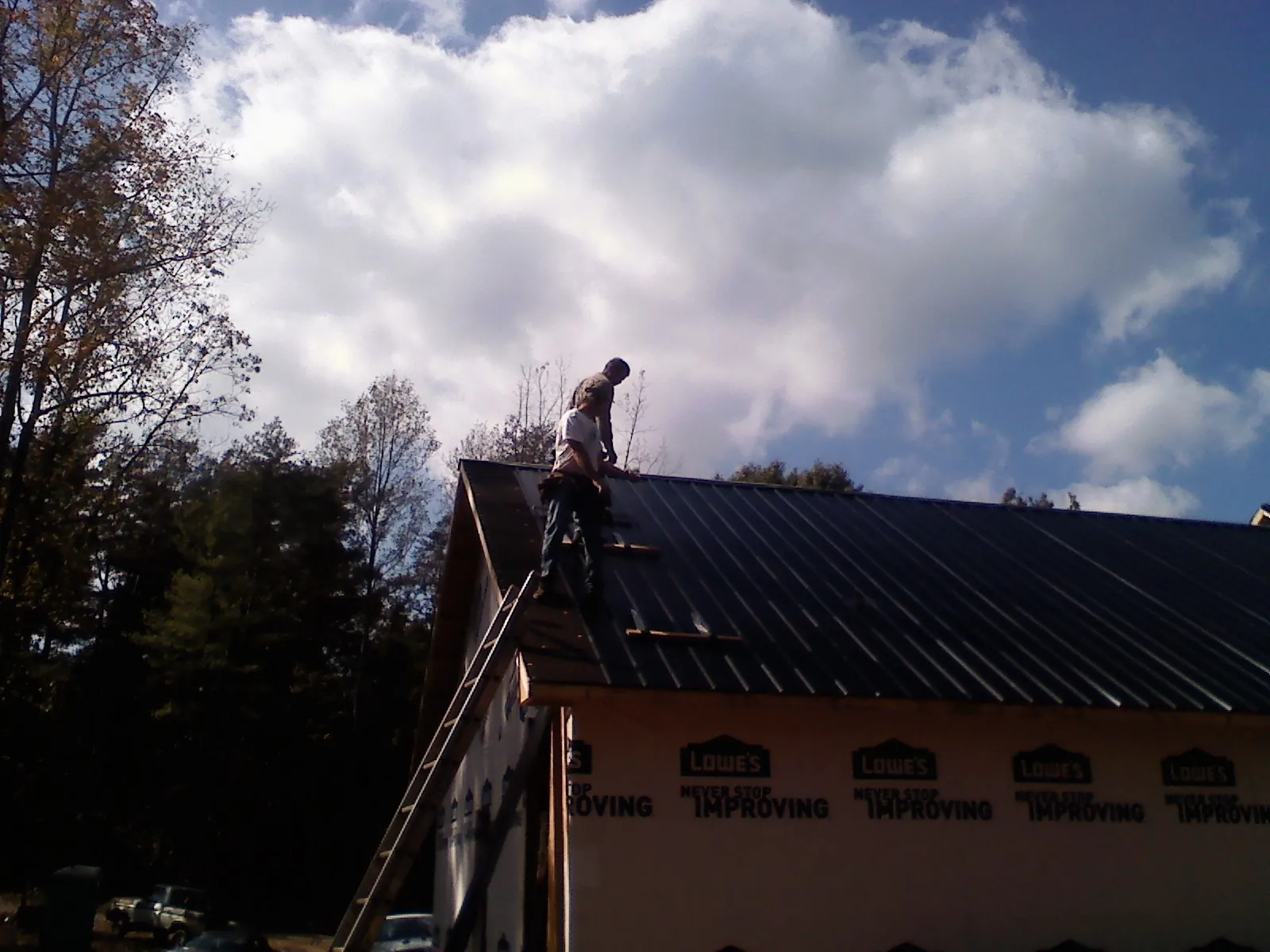 Roofer fastening dark metal panels high against a cloudy sky, from a Roof Inspection job in Cottondale