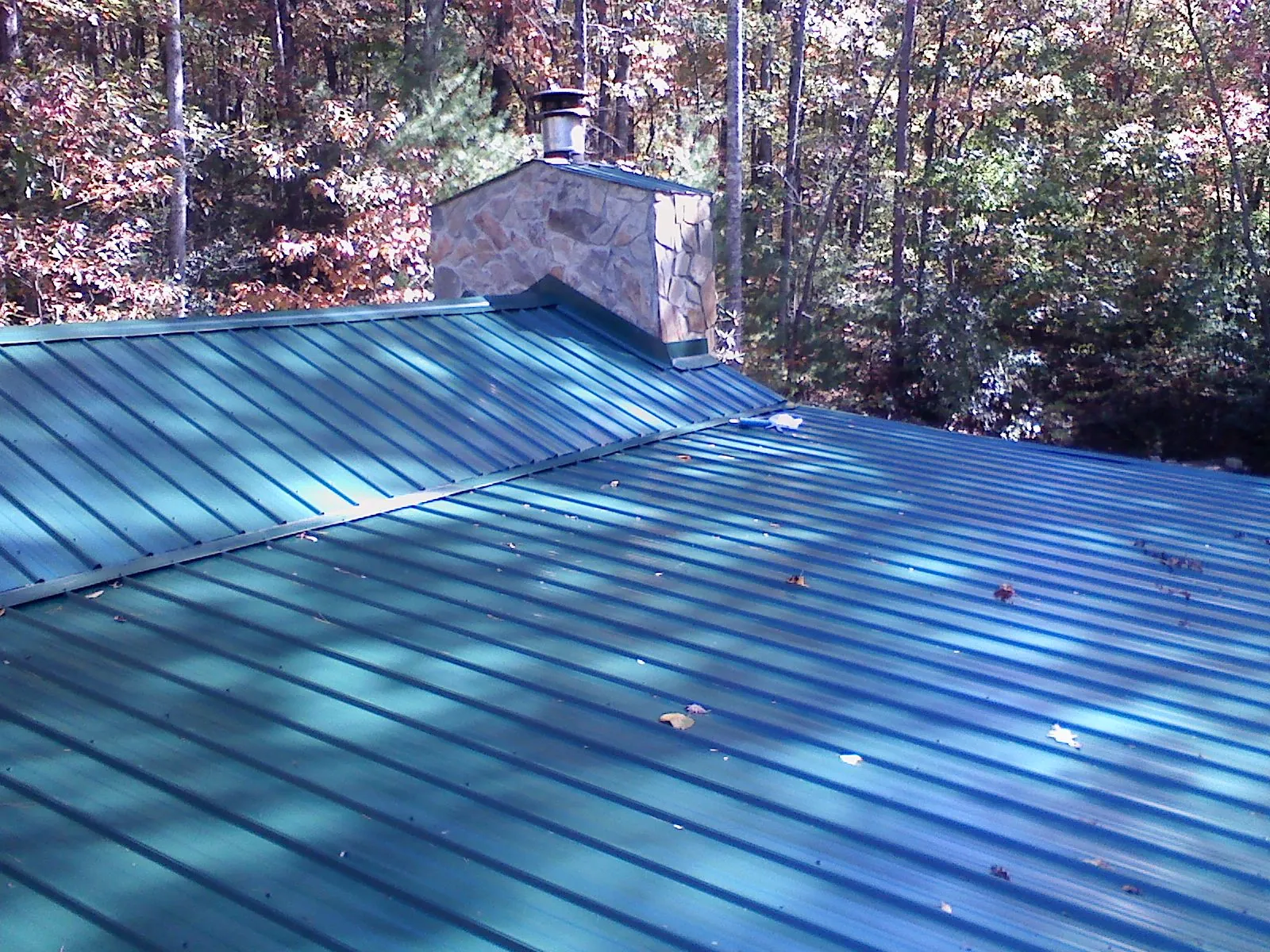 New green metal roof and stone chimney surrounded by autumn woods in Cottondale