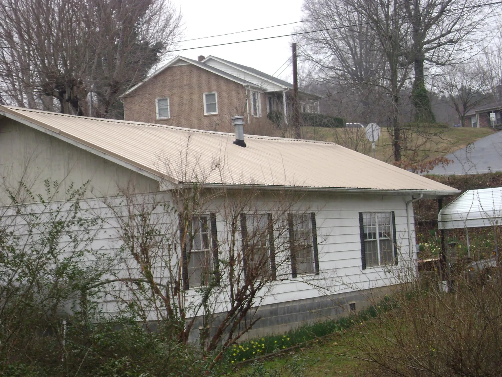 Tan metal roof on a white sided house set into a hillside — Commercial Roofing by Roofing Brothers in Cottondale